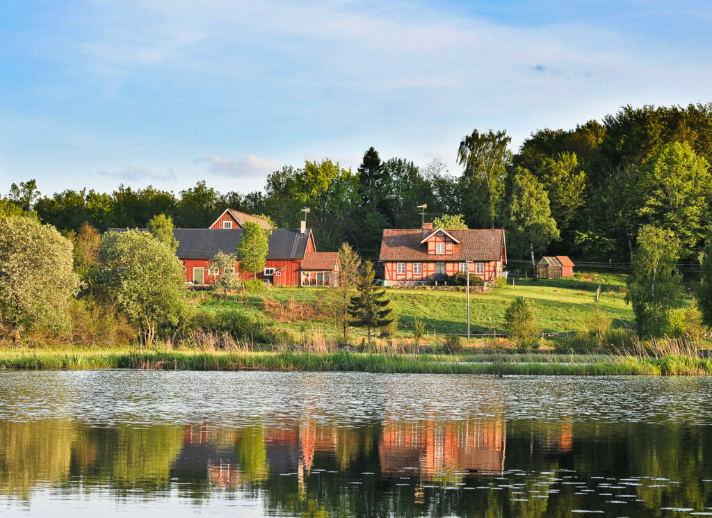 Ferienhaus in Schweden am See im Sonnenschein, umgeben von grüner Natur