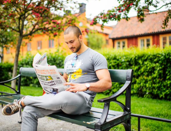 Mann liest Zeitung auf Parkbank